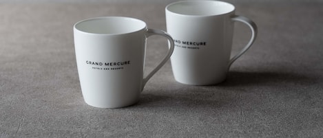 Two white mugs with 'Grand Mercure Hotels and Resorts' text, placed on a textured surface.