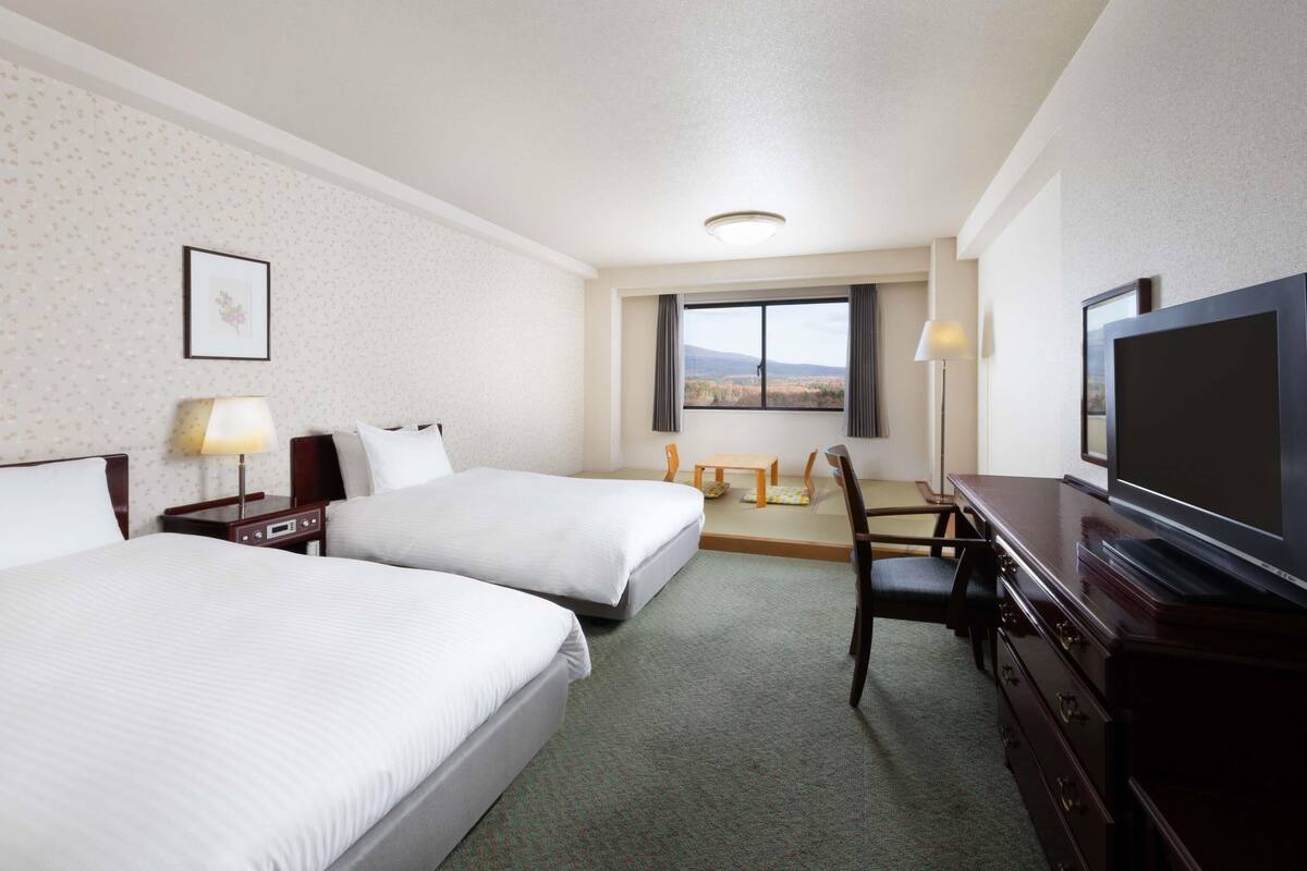 A hotel room with two beds, a desk with a chair, a television, and a window with a view.