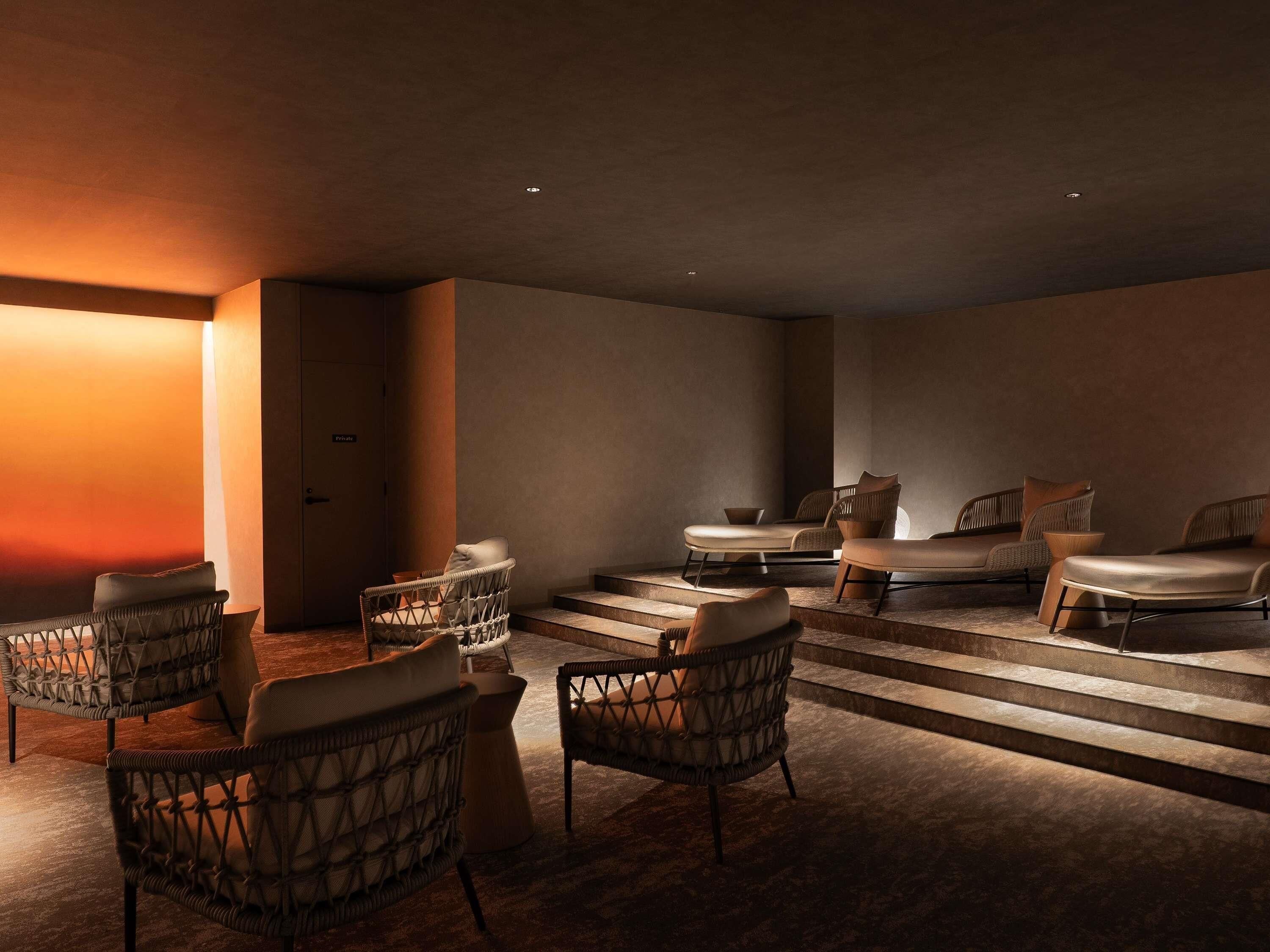 Un moderno spa con sillones de mimbre, una camilla de masaje y una escalera que conduce a una zona privada.
