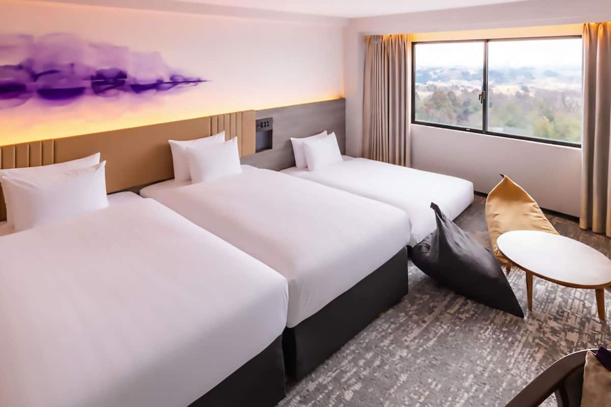 A hotel room with two beds, a sofa, a small table, and a large window with a view.