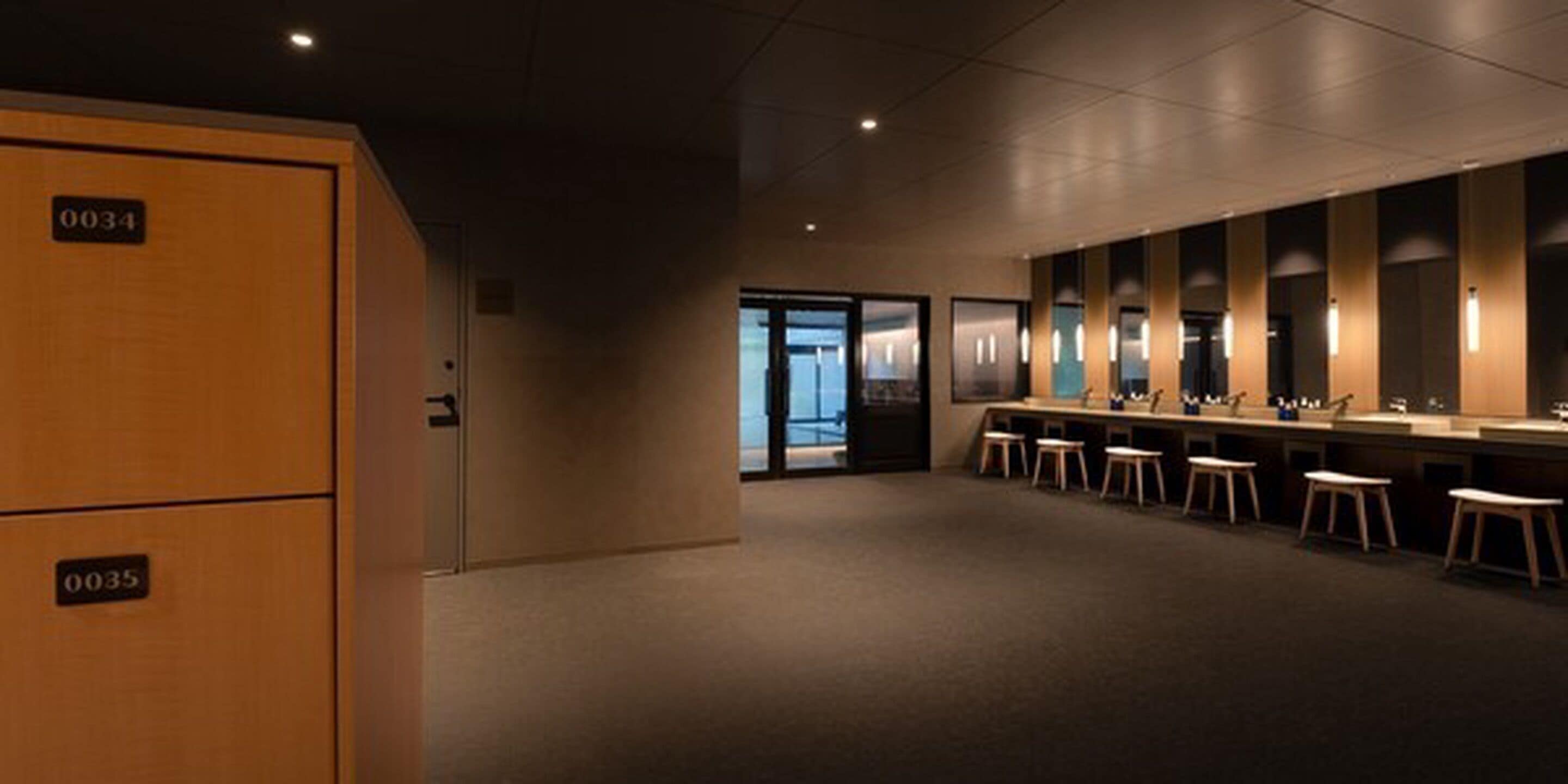 A modern hotel restroom with multiple sinks and stools, a wooden cabinet, and a dark interior.