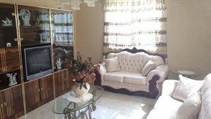 A living room with a sofa, television, and decorative items on shelves. - Sunset Oasis (Derricks)