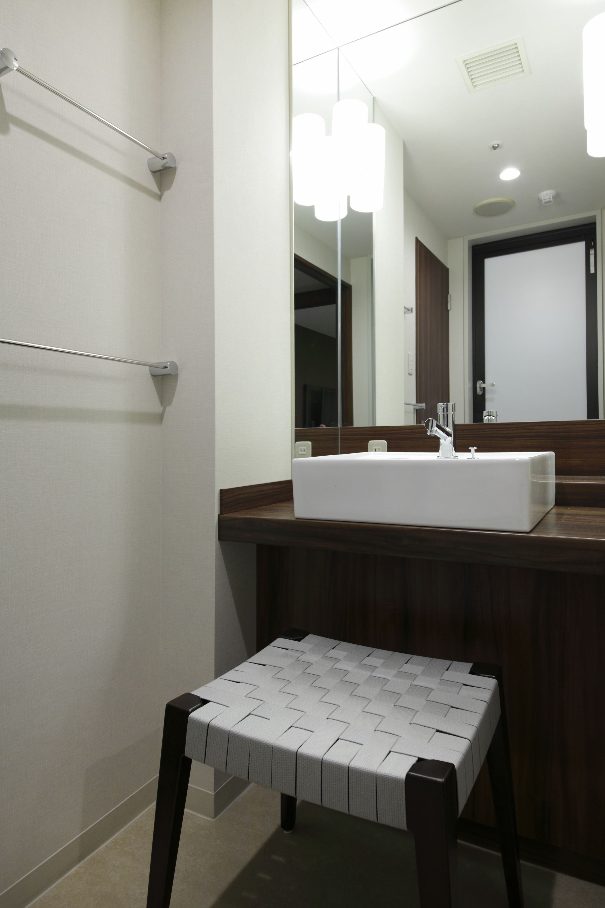 A modern bathroom with a rectangular sink, a large mirror, and a small stool.