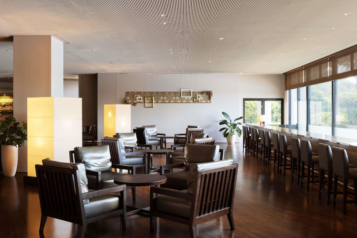A modern interior with a patterned ceiling, leather seating, a long table, and large windows.