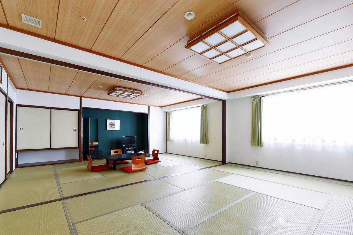 A tatami mat room with a television, tatami mats, a table, chairs, and sliding doors.