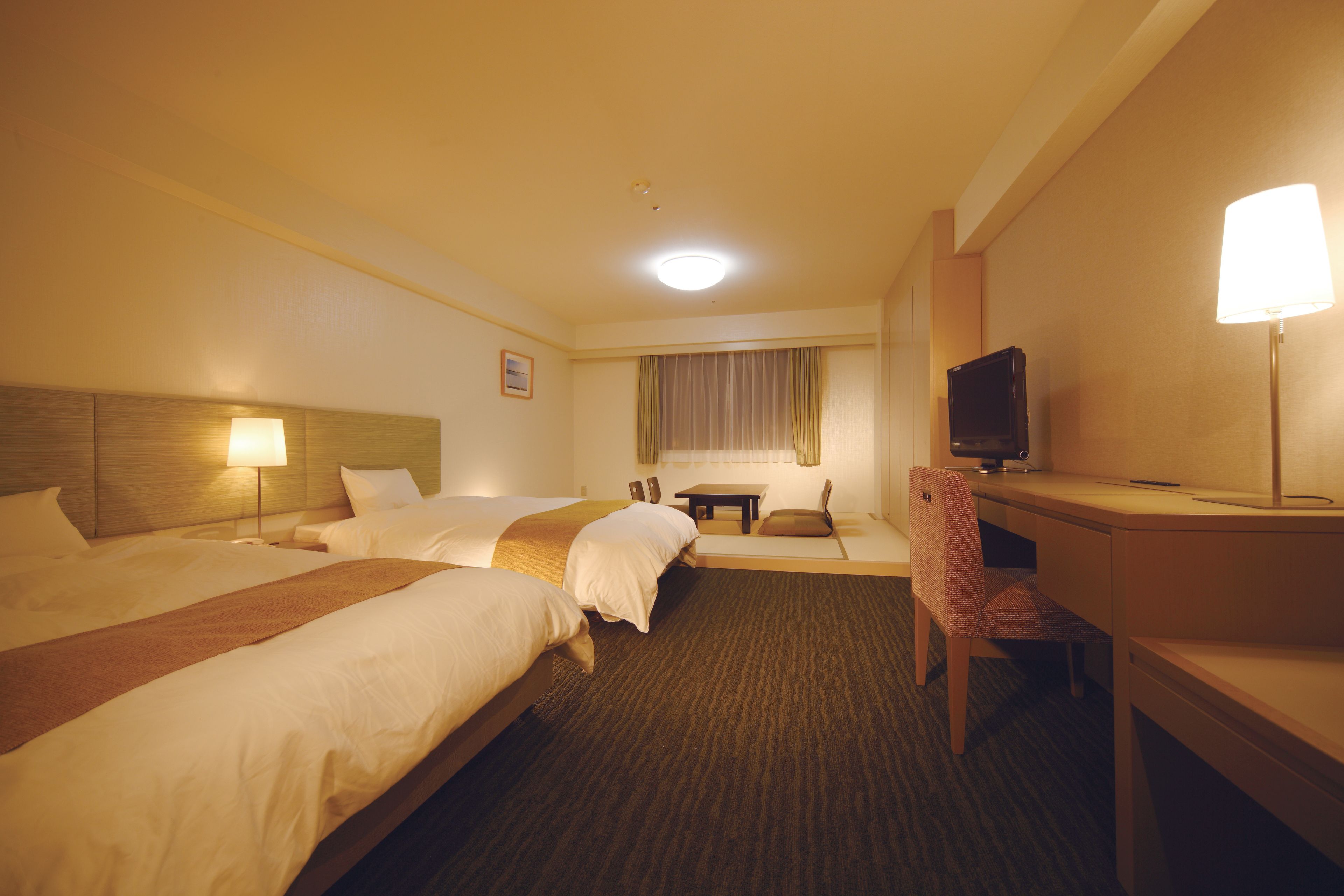 Une chambre d’hôtel avec deux lits, un bureau, une chaise, une télévision et une lampe.