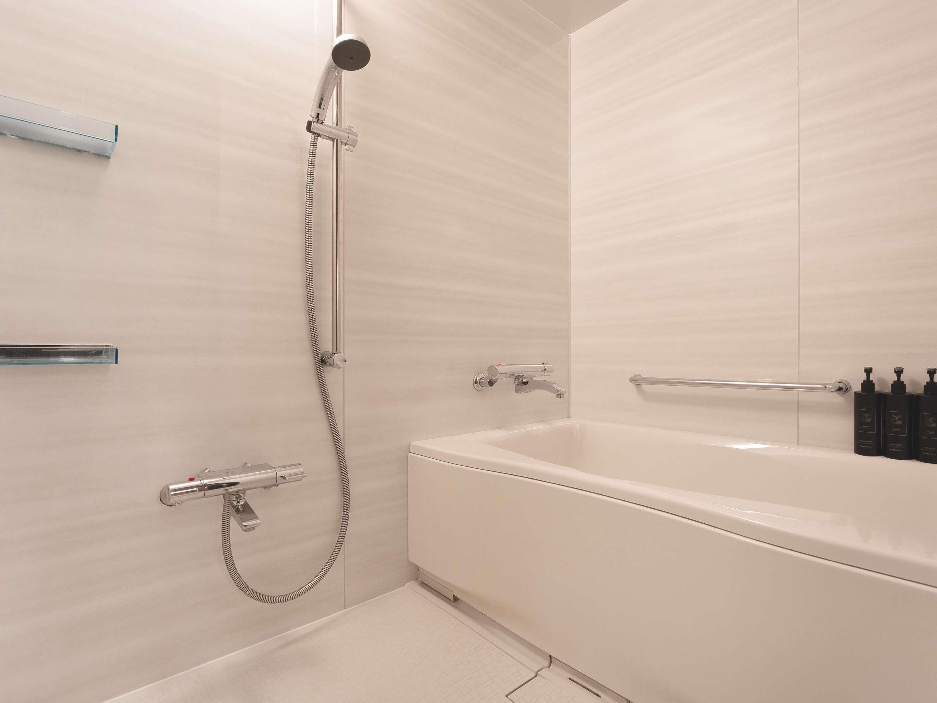 A modern bathroom with a bathtub, shower, and handrails.