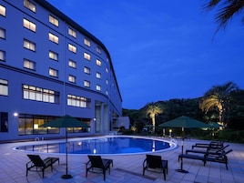 Un hotel con piscina, mobiliario exterior y un edificio grande con muchas ventanas.