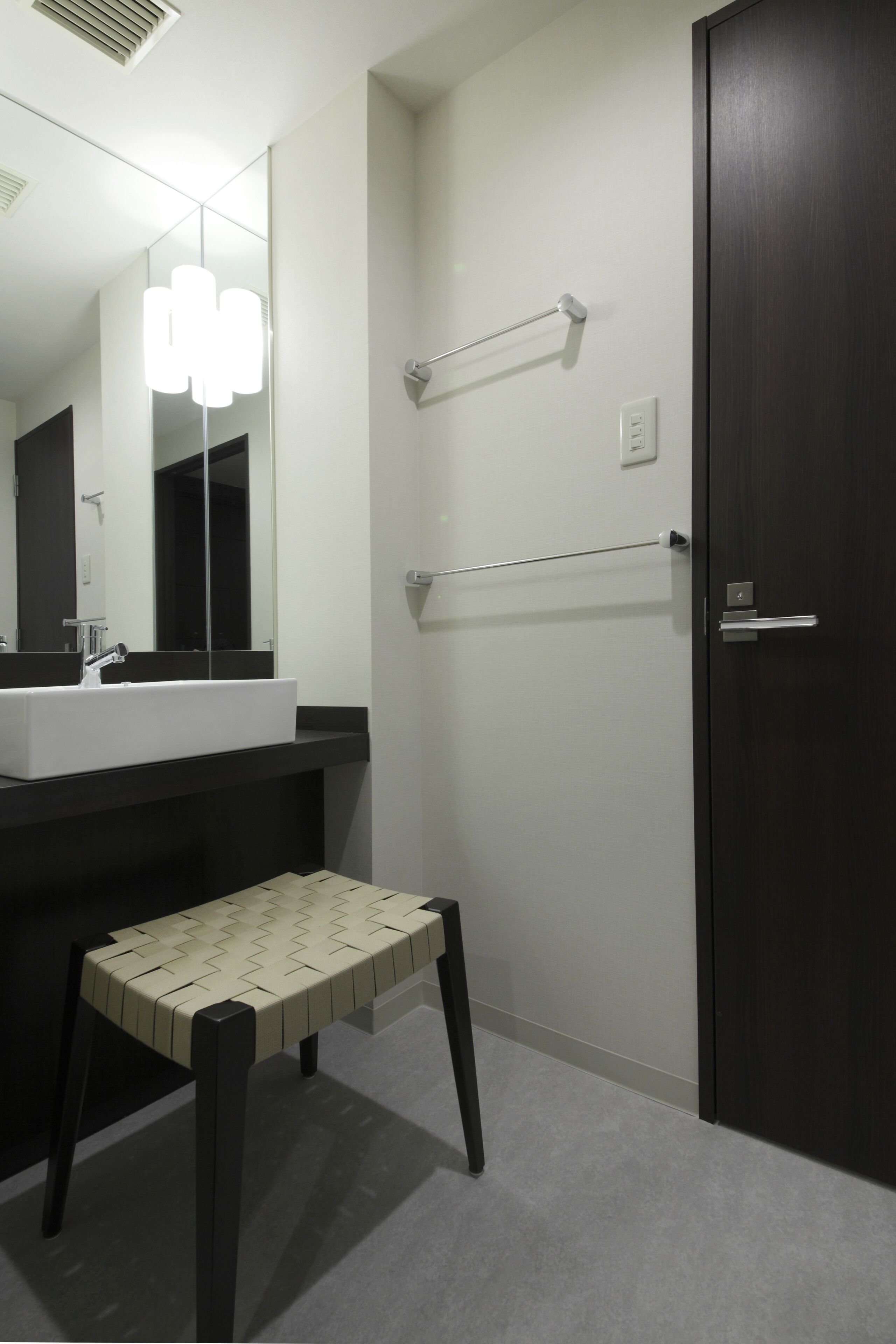 A modern bathroom with a white sink, dark wooden door, and a small stool.