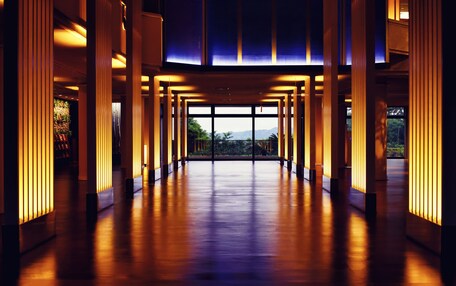 A spacious corridor with a view of the outdoors, featuring tall columns and a wooden floor.