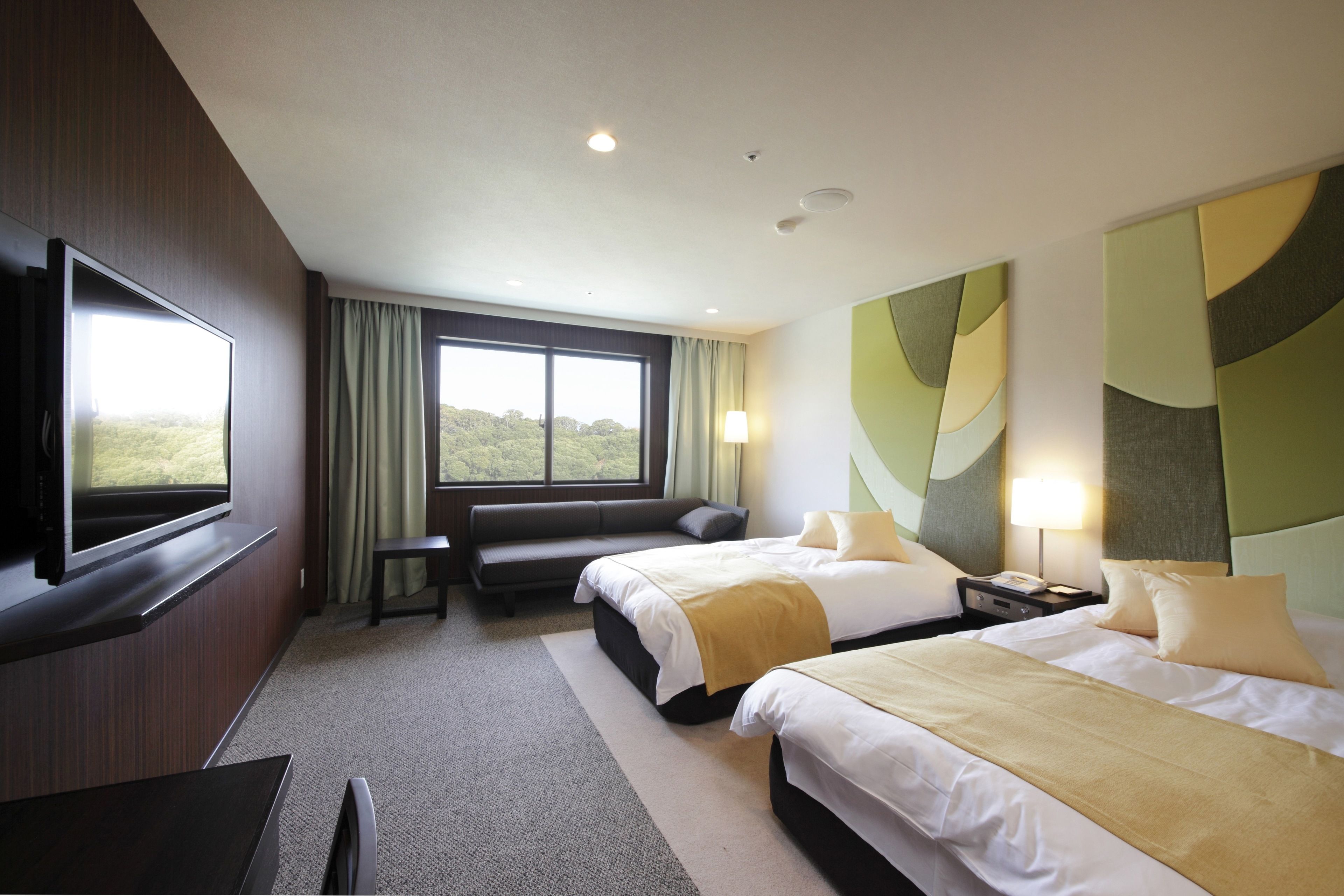 A hotel room with two beds, a TV, a sofa, and a large window with a view.