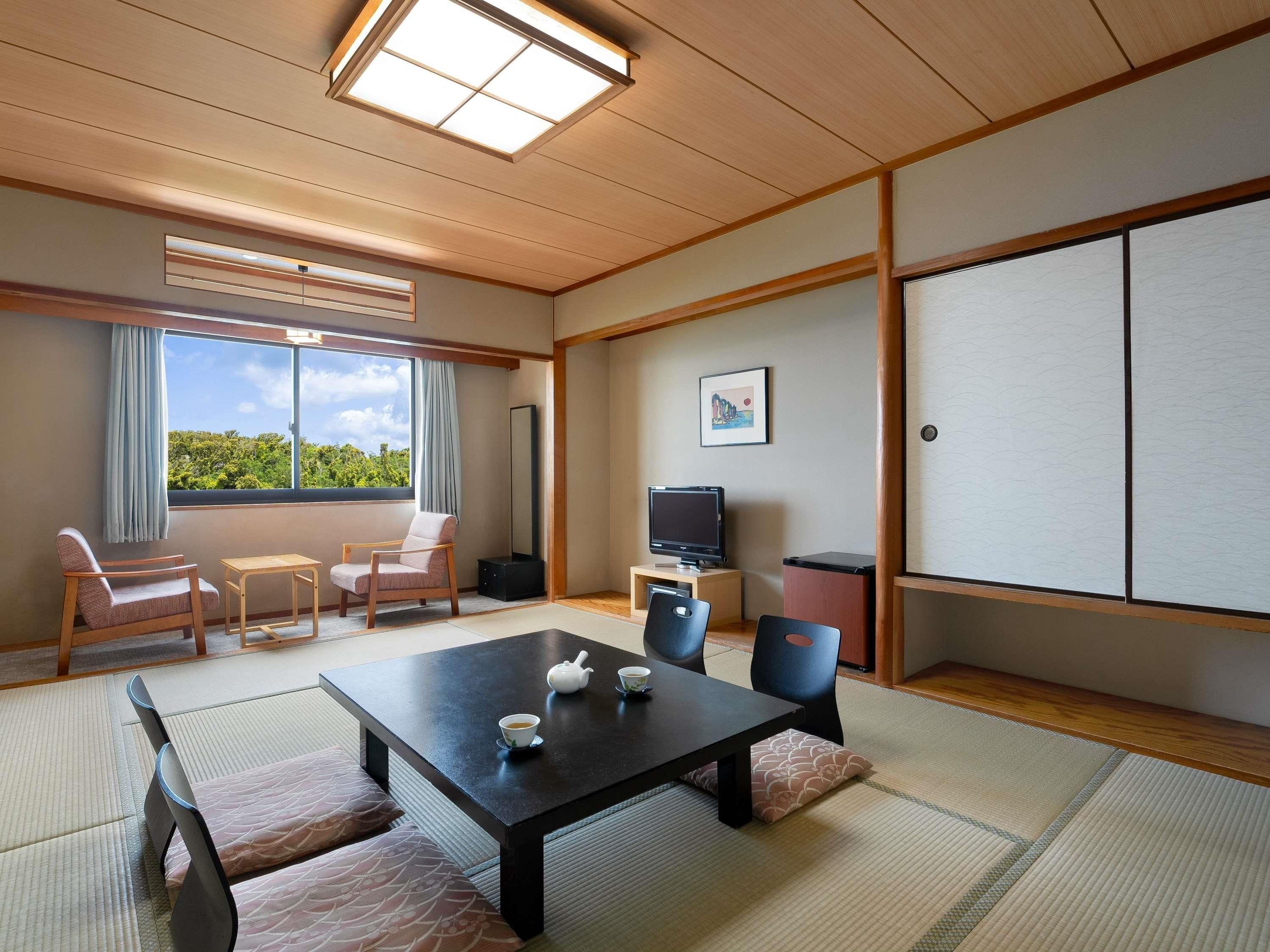 Een traditionele Japanse kamer met tatami vloerbedekking, een lage tafel met theepot, stoelen, een televisie en een grote shoji schuifwand.