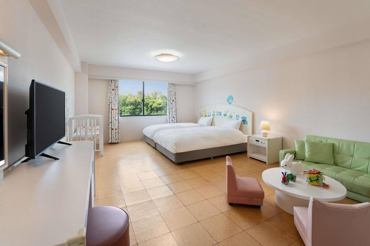A hotel room with a bed, a desk with a TV, a green sofa, and a small table with toys.
