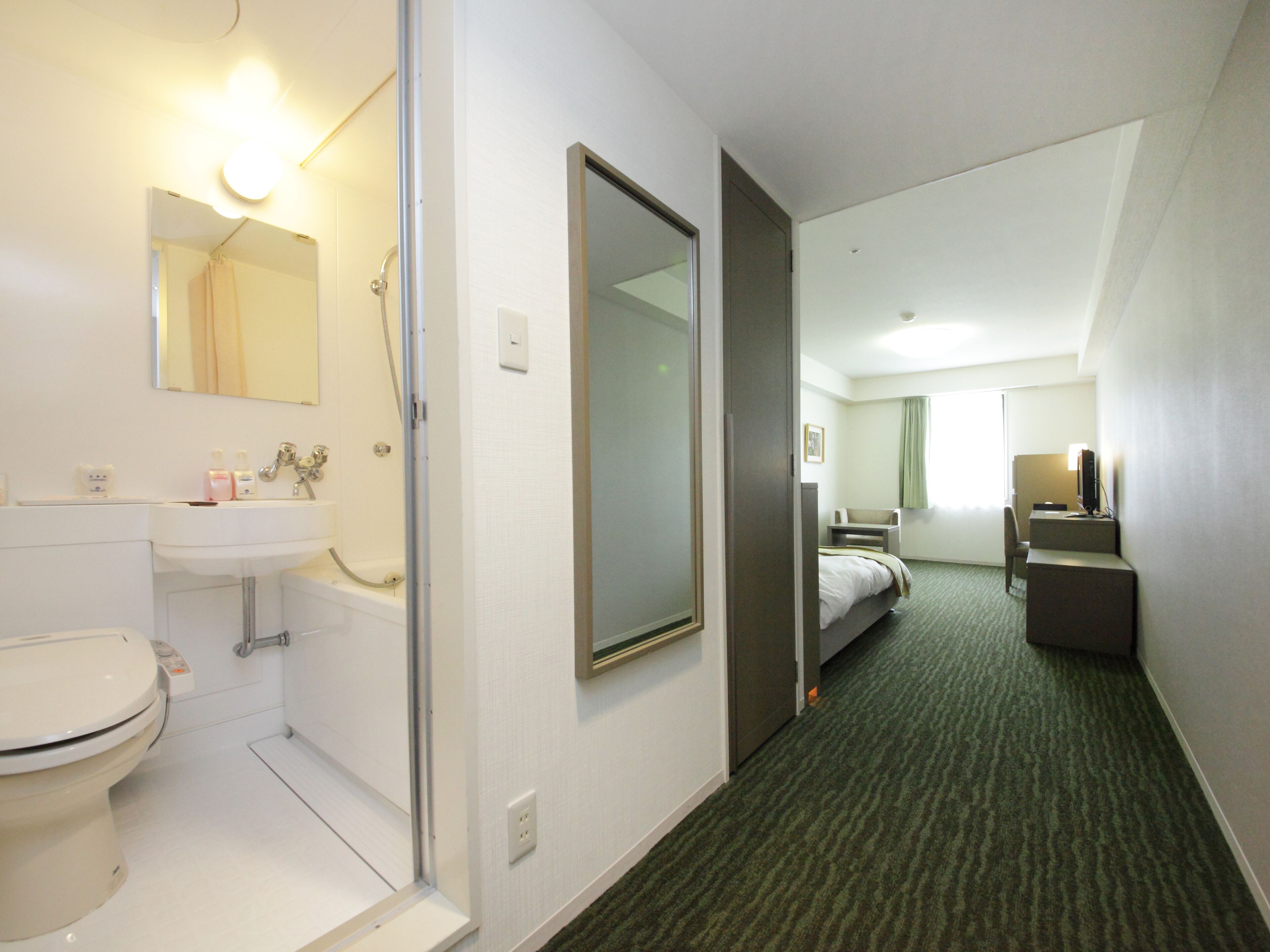 A hotel room with a bathroom, a bed, a desk, and a television.