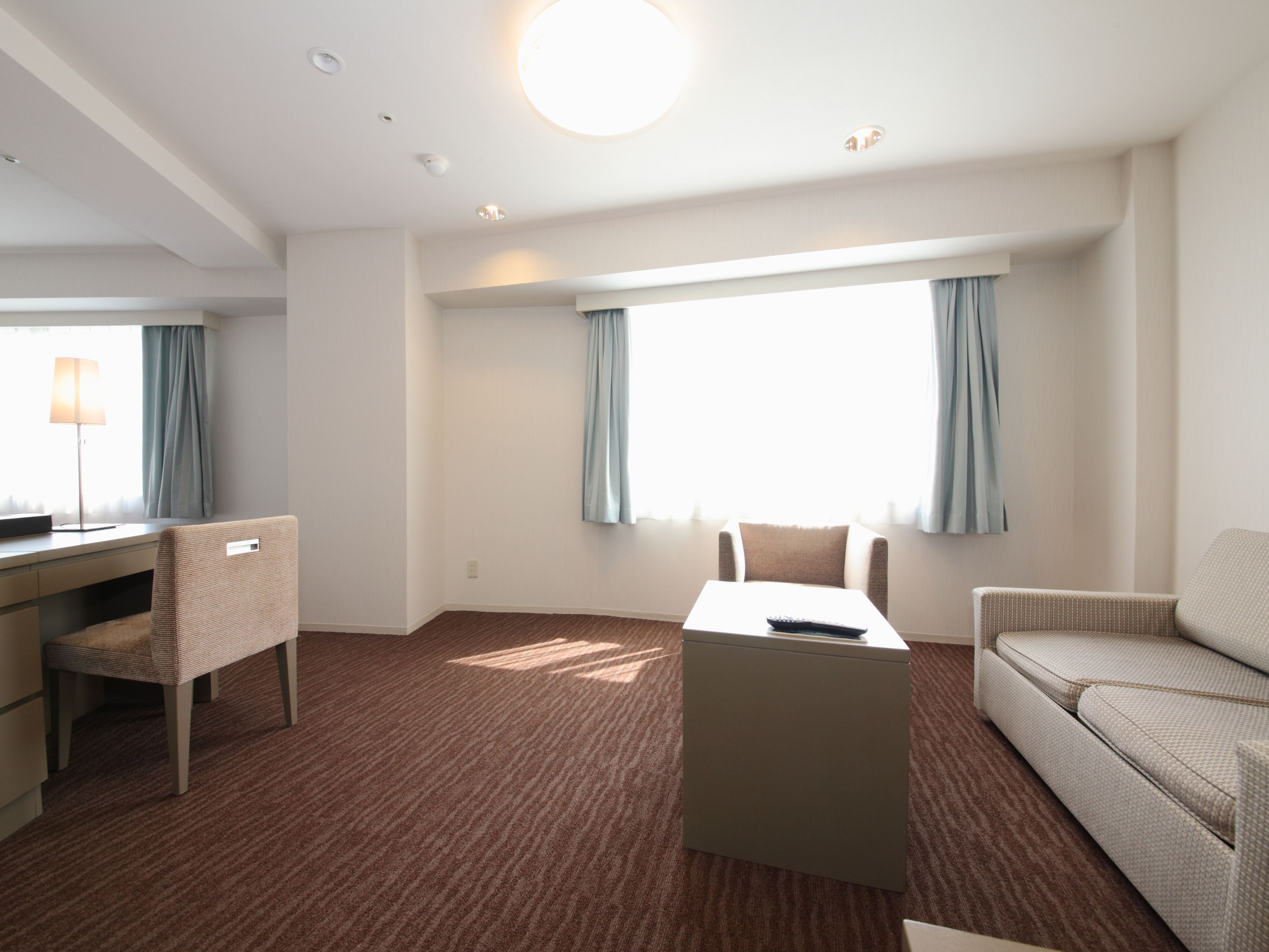 A modern hotel room with a flat-screen TV, a sofa, a chair, and a coffee table.