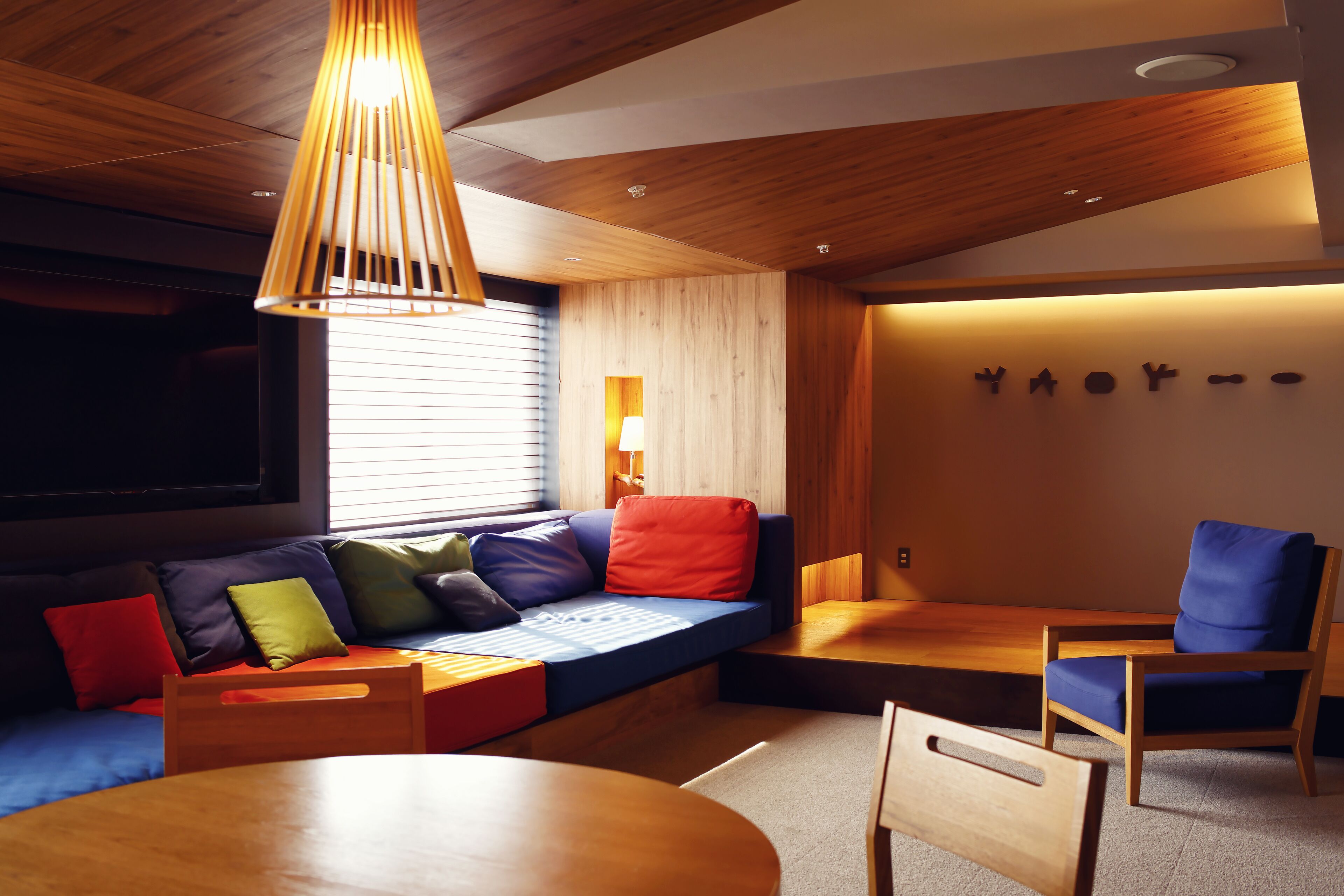 A modern interior with a wooden ceiling, a blue sofa with colorful cushions, a wooden table, and a blue chair.