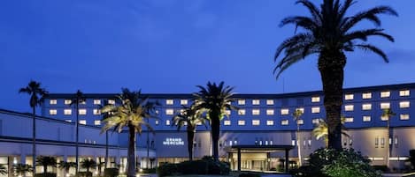 A hotel with a large building, palm trees, and a well-lit entrance.
