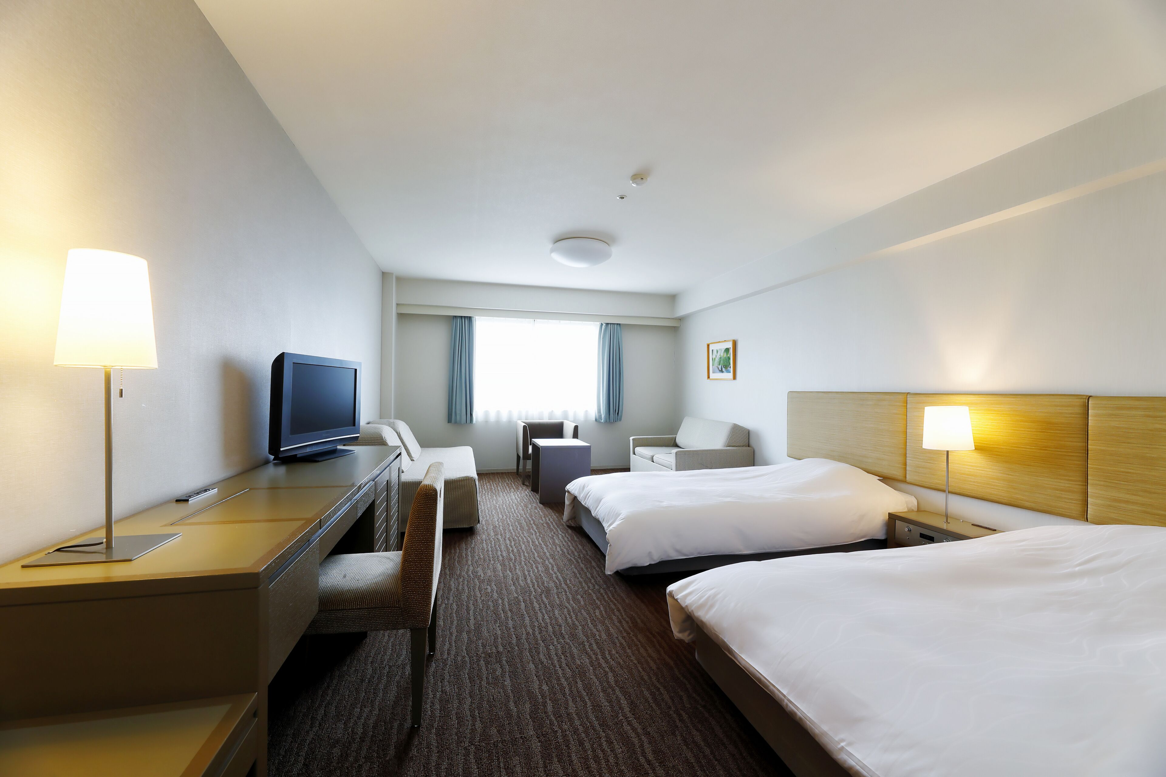 A hotel room with two beds, a desk with a computer, a chair, a TV, and a lamp.