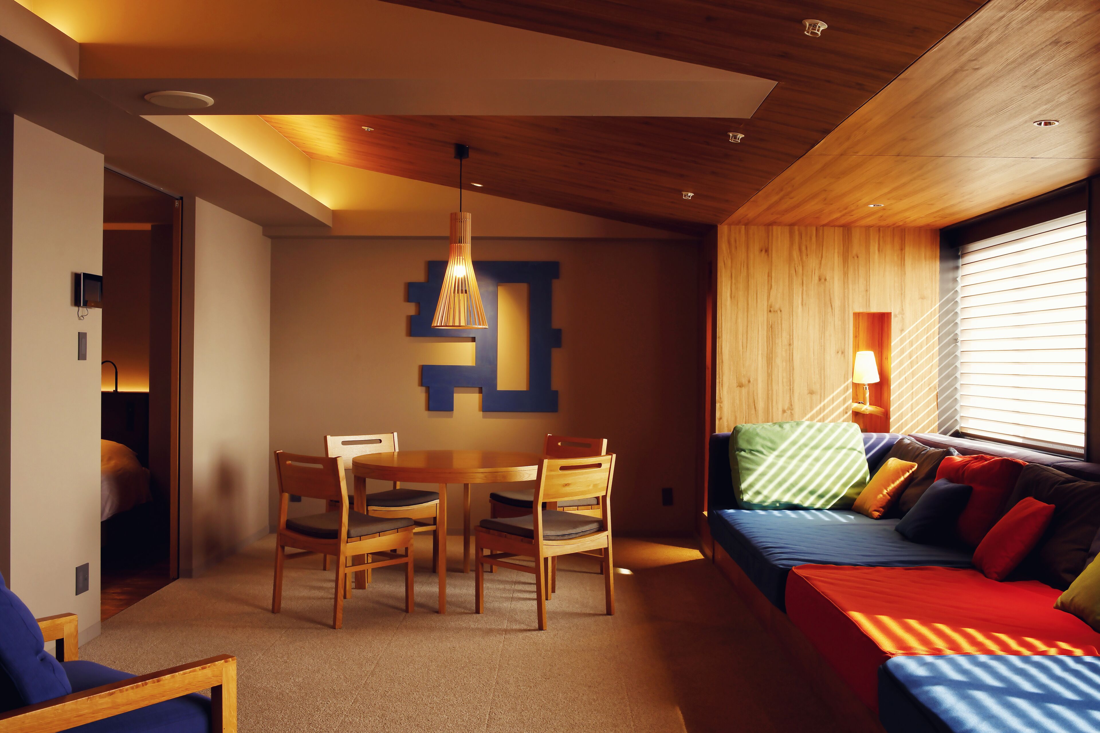 A modern room with a wooden ceiling, a dining area with a table and chairs, and a sofa with colorful cushions.