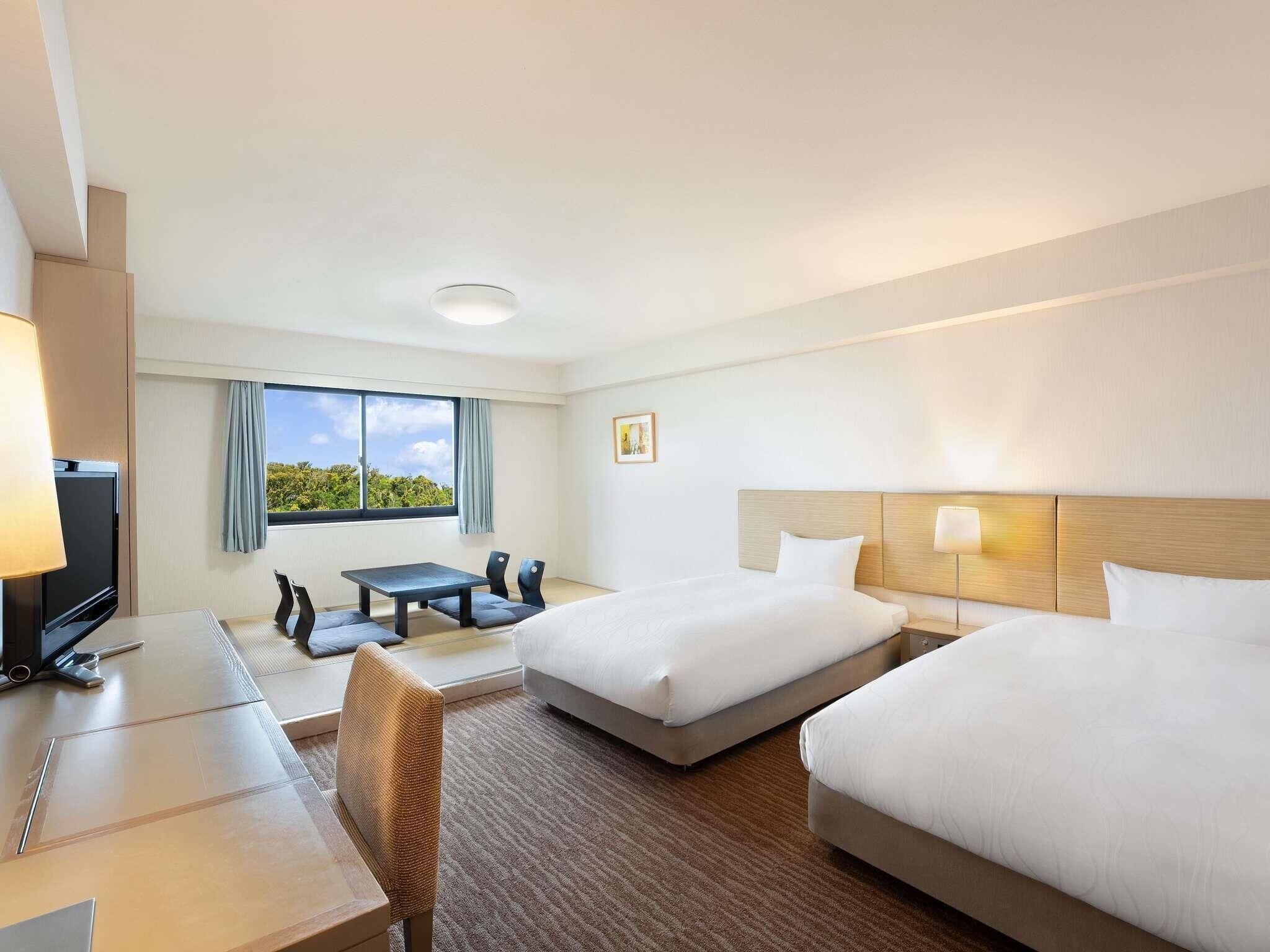 Une chambre d’hôtel avec deux lits, un bureau, une chaise, une télévision et une fenêtre donnant sur un paysage agréable.