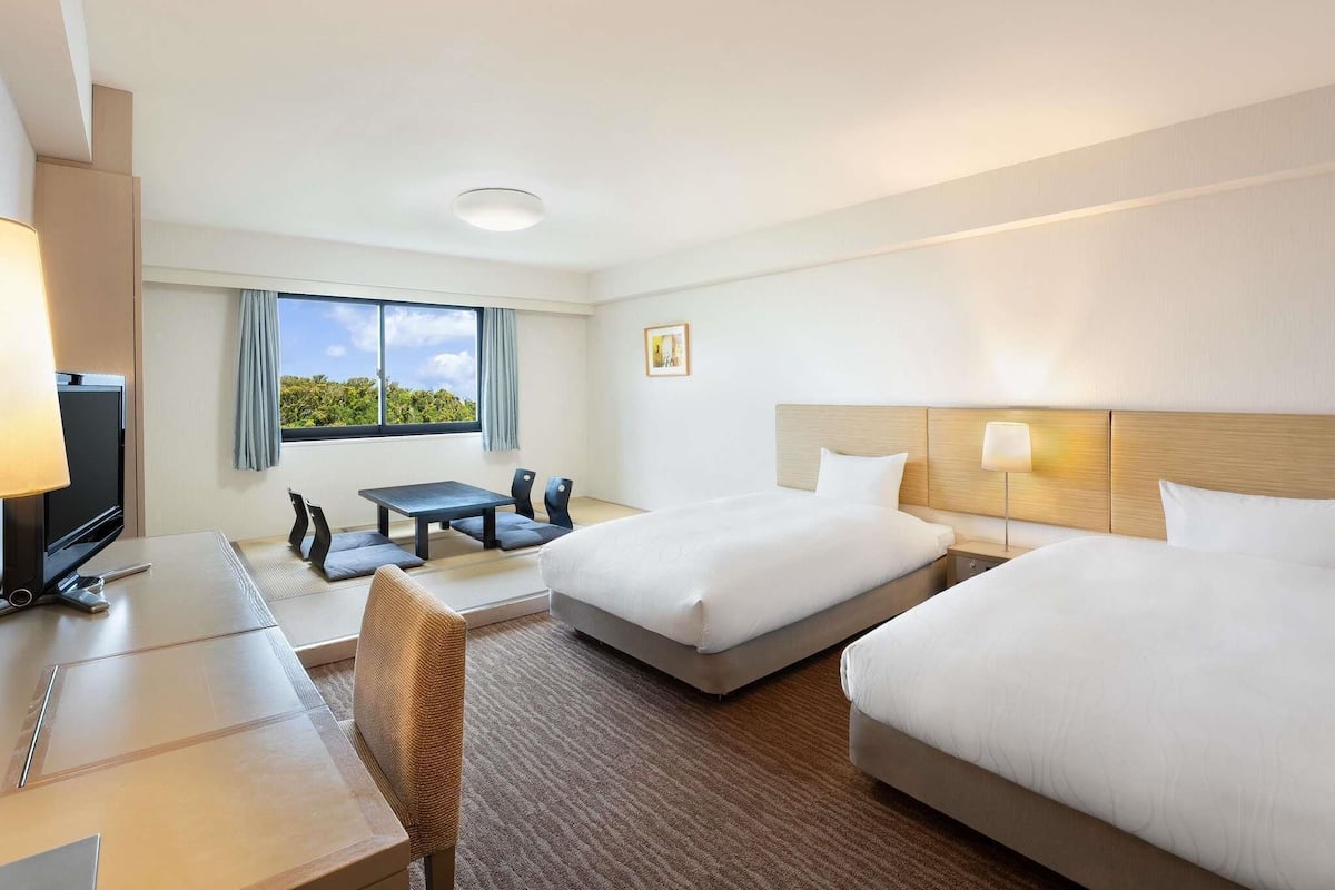 Une chambre d’hôtel avec deux lits, un bureau, une chaise, une télévision et une fenêtre donnant sur un paysage agréable.