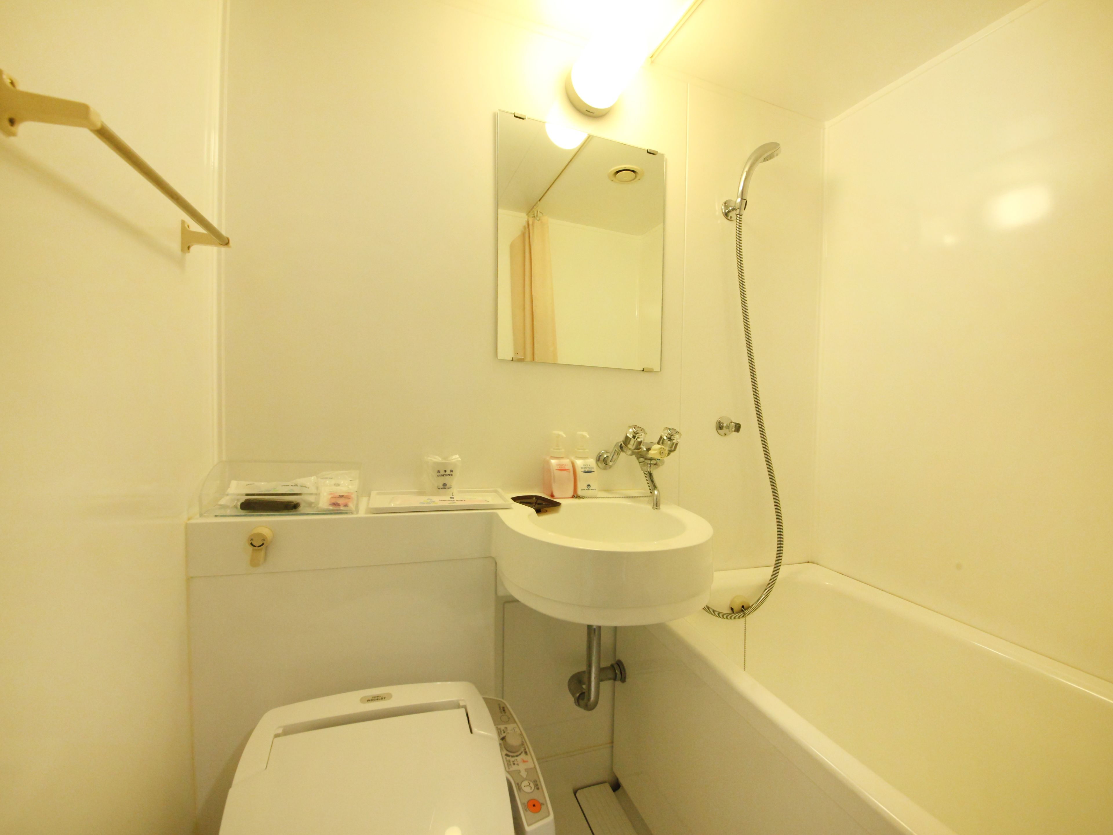 A small, compact bathroom with a white sink, a mirror, a shower, and a toilet.