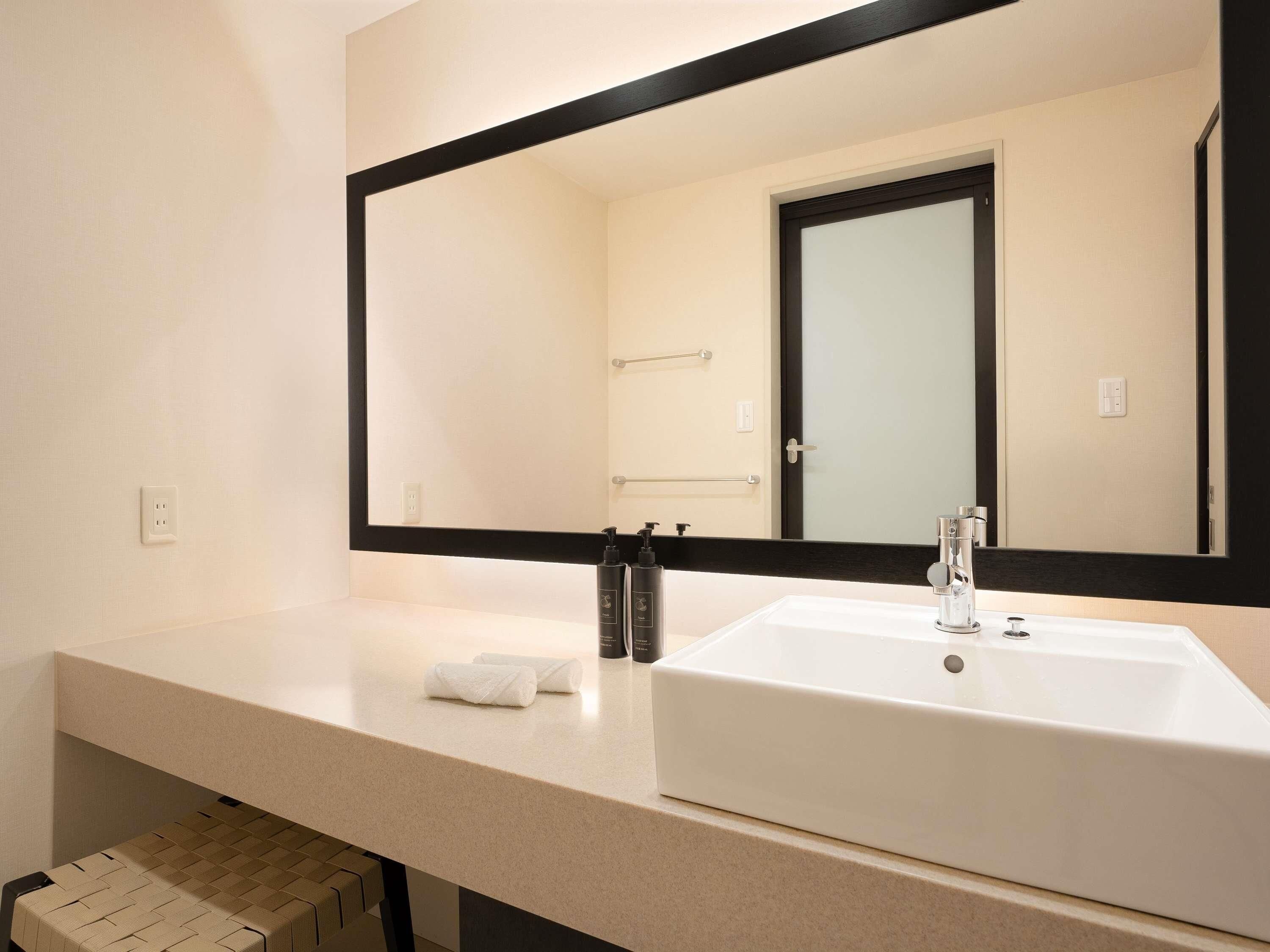 A modern bathroom with a large mirror, a white sink, and a towel on the counter.