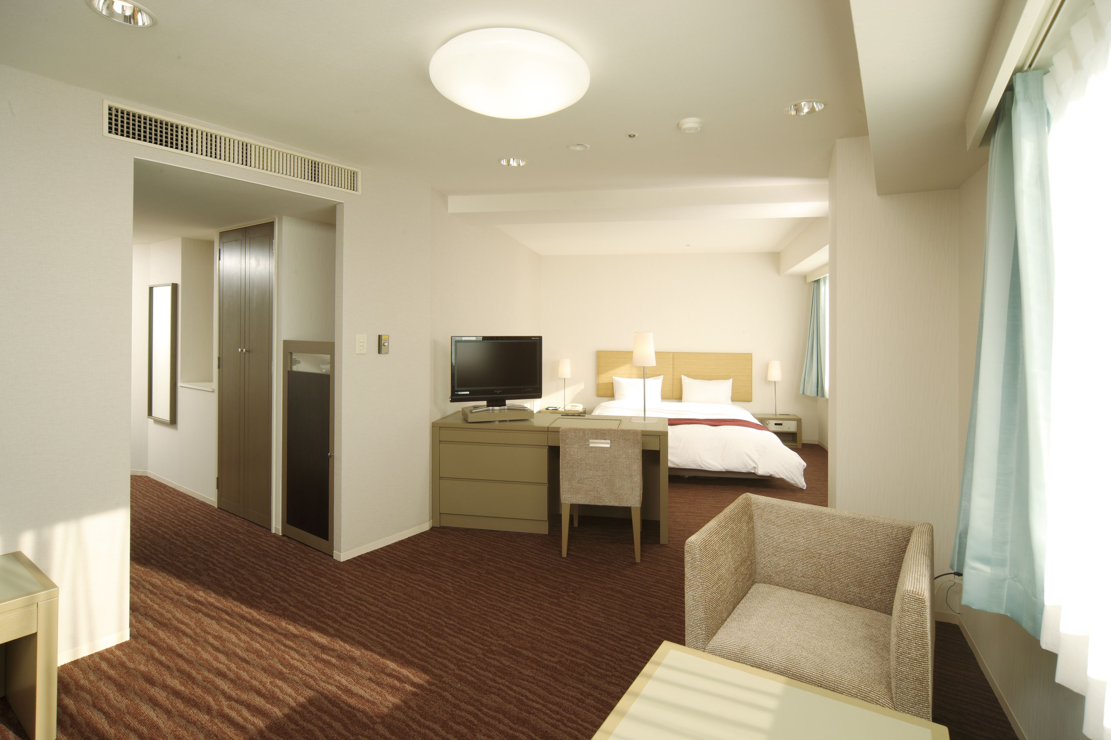 Ein Hotelzimmer mit Bett, Schreibtisch, Stuhl, Fernseher und einem Fenster mit Vorhängen.