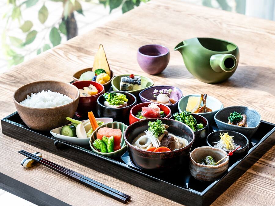 Variedad de platos japoneses dispuestos en una bandeja, incluyendo arroz, verduras y carne, junto con palillos y recipientes pequeños.