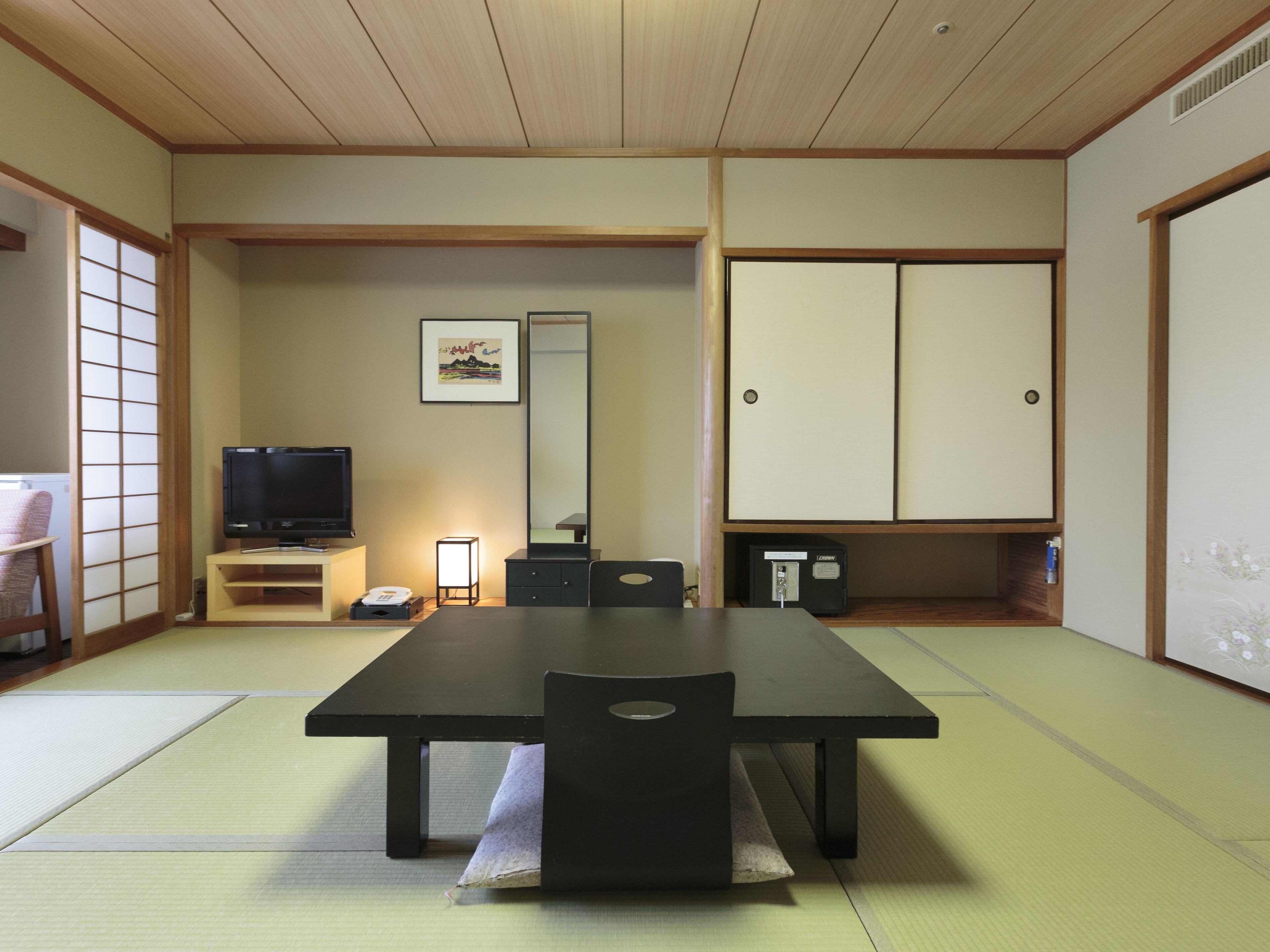 Una habitación tradicional japonesa con suelo de tatami, una mesa baja, un televisor, un armario y un cuadro en la pared.