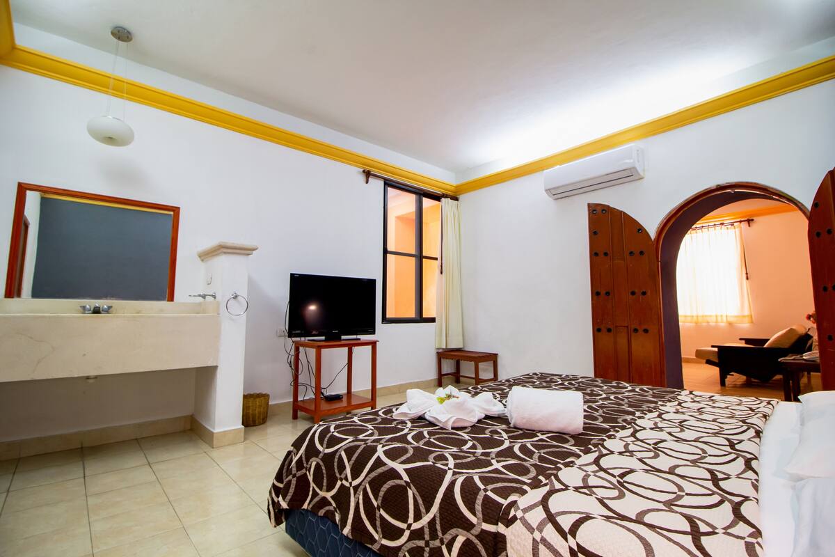 A hotel room with a bed, a TV, a bathroom with a mirror, and a wardrobe.