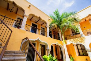 A yellow building with a staircase, balconies, and a palm tree.