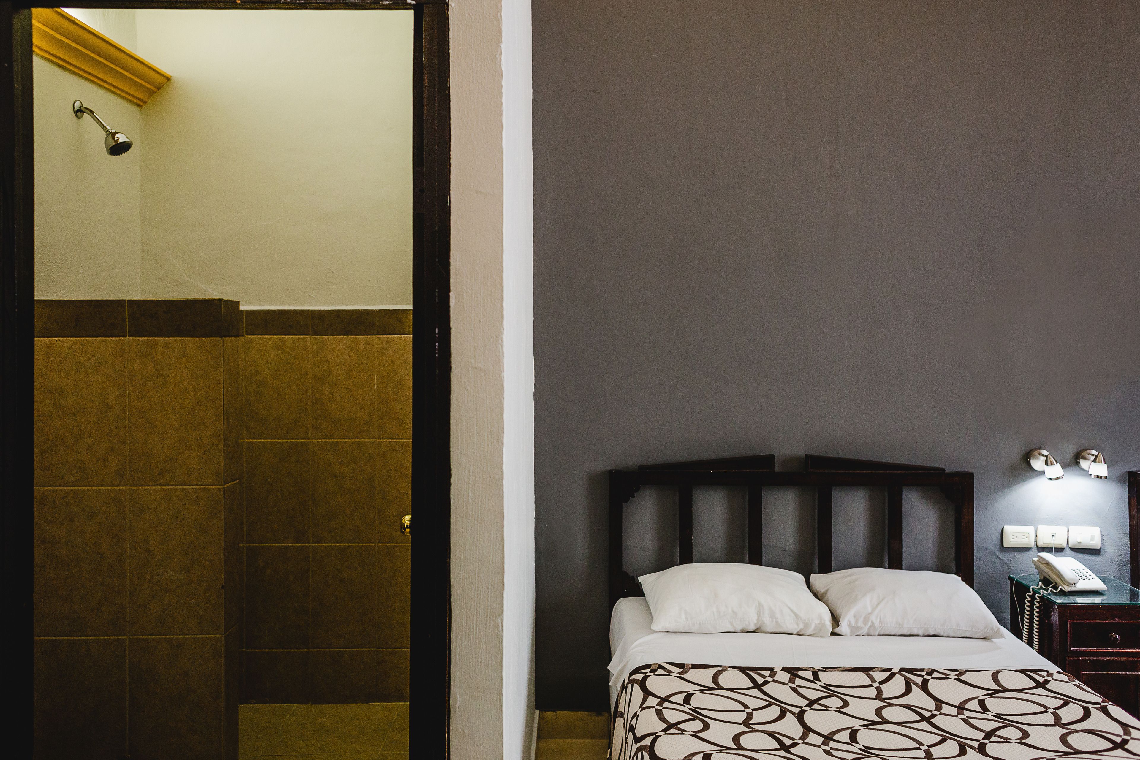 A hotel room with a bed, bedside table, and a nightstand with a phone.