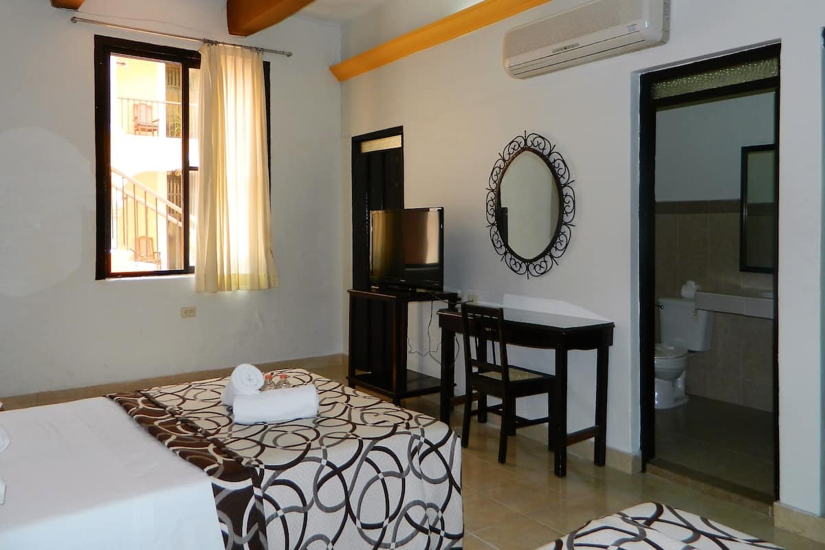 A hotel room with a bed, a desk with a chair, a television, a bathroom with a toilet, and a large mirror.