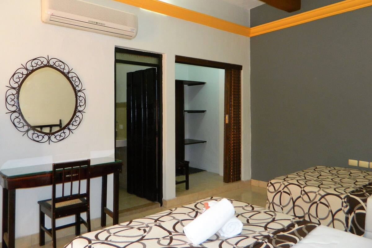 A hotel room with a desk, chair, two beds, a mirror, and a wardrobe.
