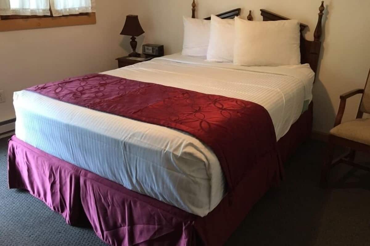 A neatly made bed with a red and white bedspread, a wooden headboard, and a nightstand with a lamp and clock.
