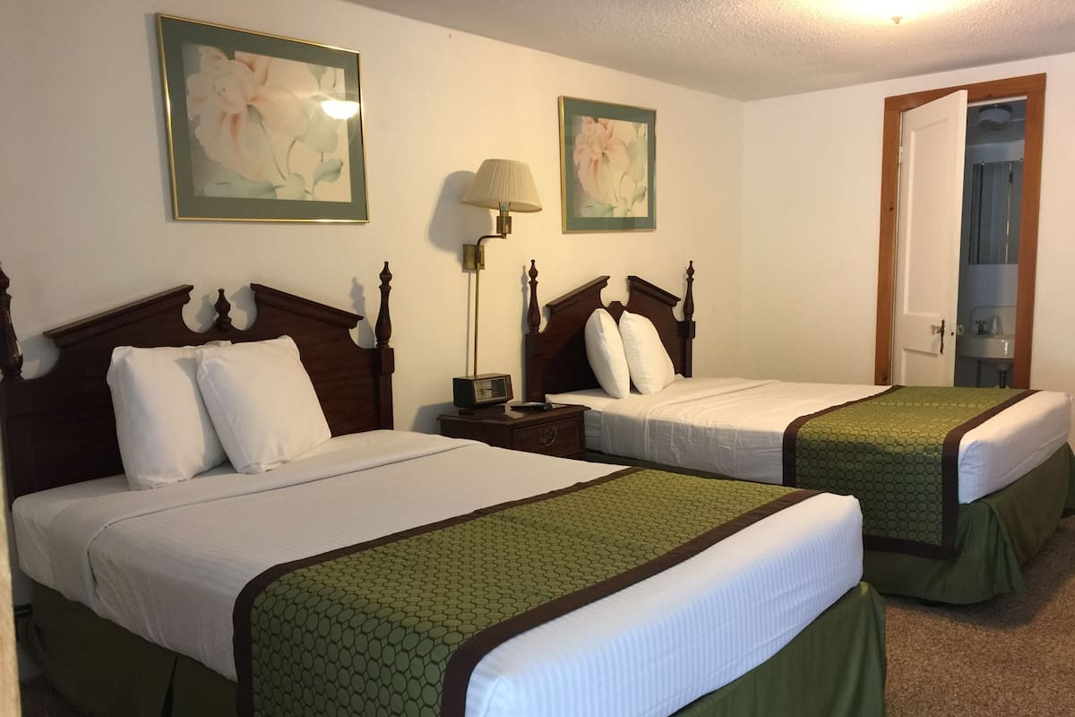 Two double beds with wooden headboards, a bedside table with a lamp, and a framed floral artwork on the wall.
