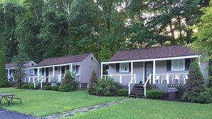 A row of single-story mobile homes with attached porches, surrounded by lush greenery. - Adirondack Oasis Motel (Lake George)
