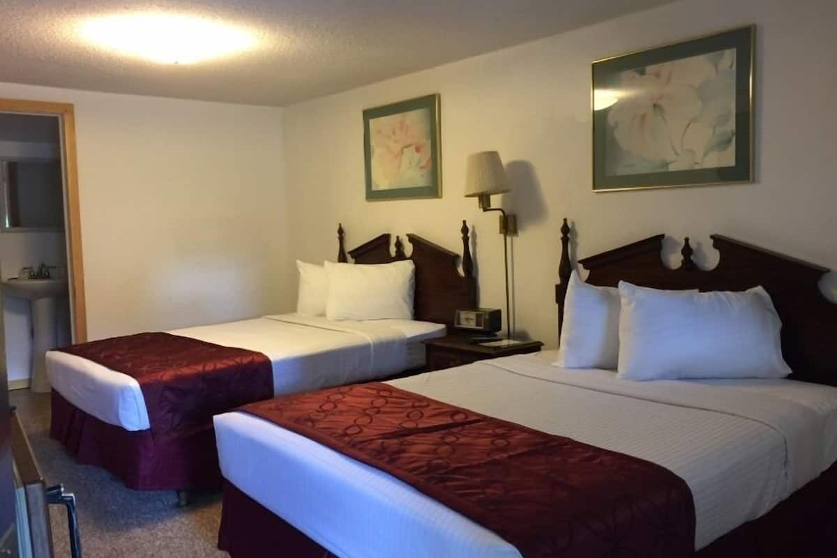 A hotel room with two single beds, a nightstand with a lamp, a mirror, and two framed pictures on the wall.