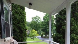 A wooden porch with white railings, two white plastic chairs, and a small table. - Adirondack Oasis Motel (Lake George)