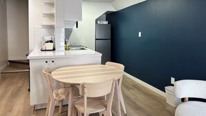A compact kitchen with a white countertop, a sink, and a built-in refrigerator. There is a round wooden dining table with chairs. The walls are painted in two colors, one dark and one light. - Cloud 9 Inn (Whitecourt)