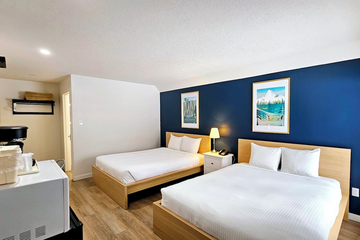 A hotel room with two single beds, a desk with a computer, a chair, and a refrigerator.