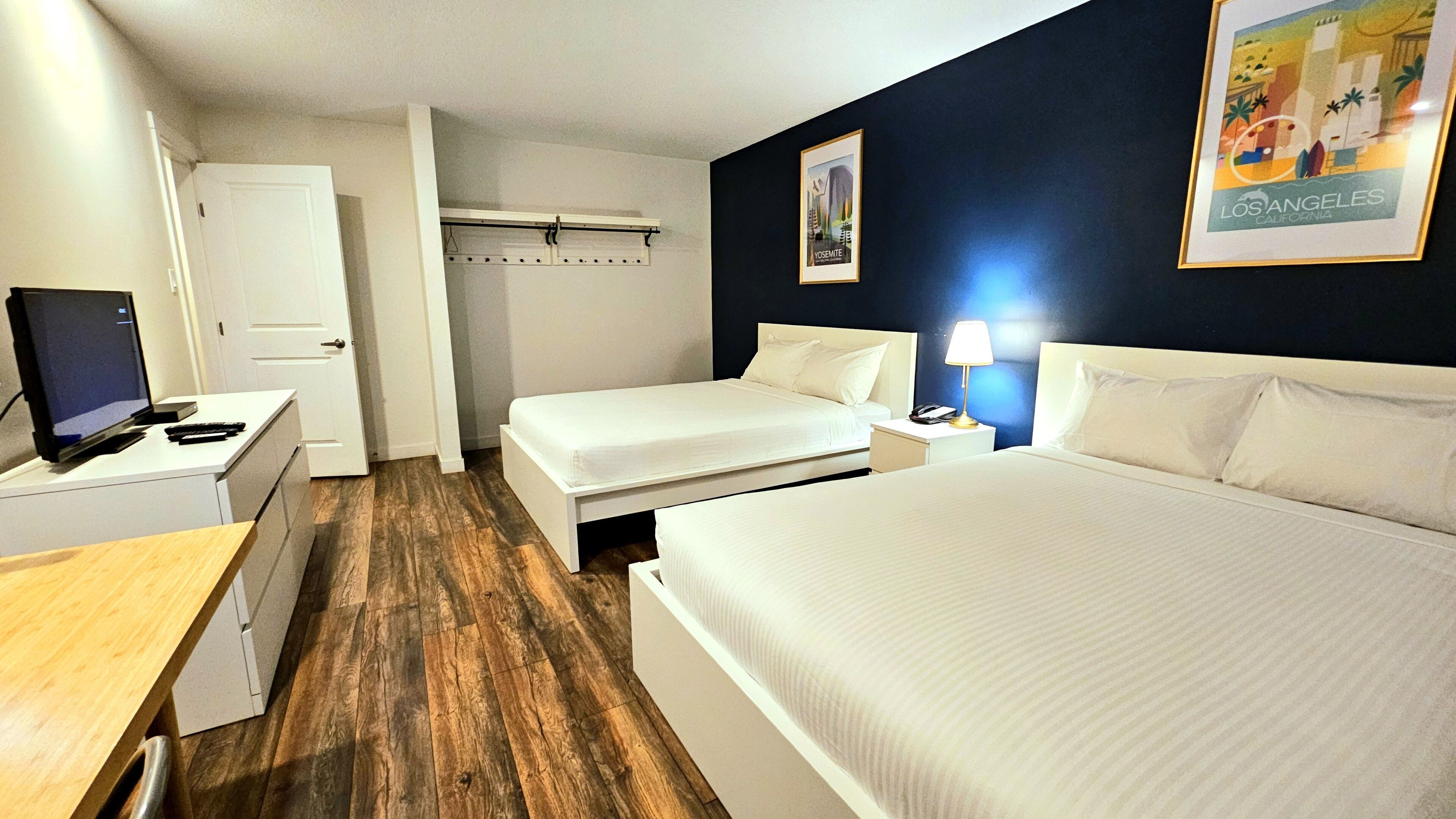 A hotel room with a large bed, a smaller bed, a desk with a computer, and a wardrobe.