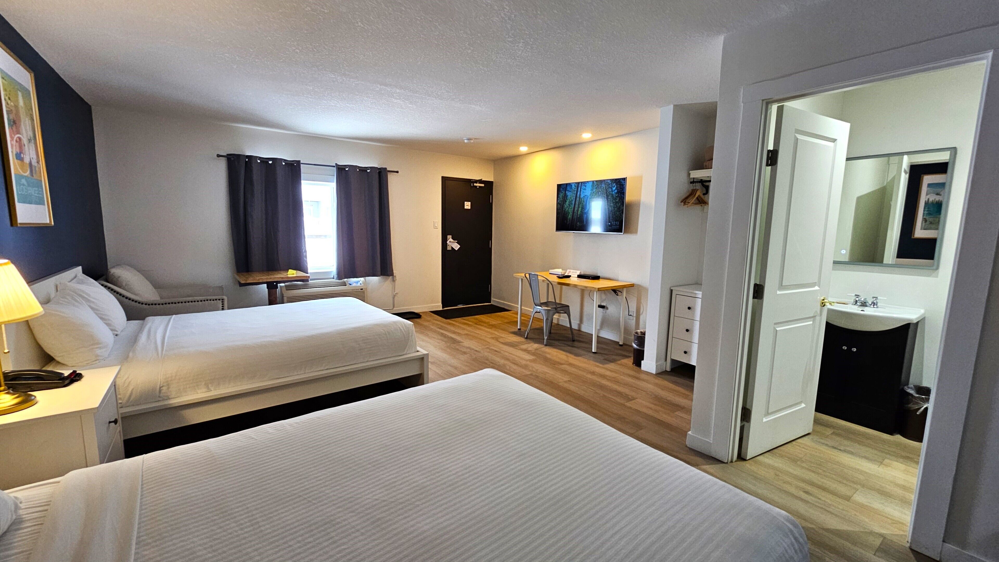A hotel room with two beds, a desk, a chair, a TV, and a bathroom.