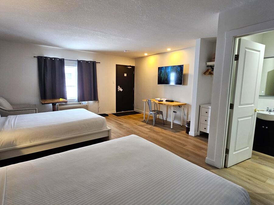 A hotel room with two beds, a desk, a chair, a TV, and a bathroom.