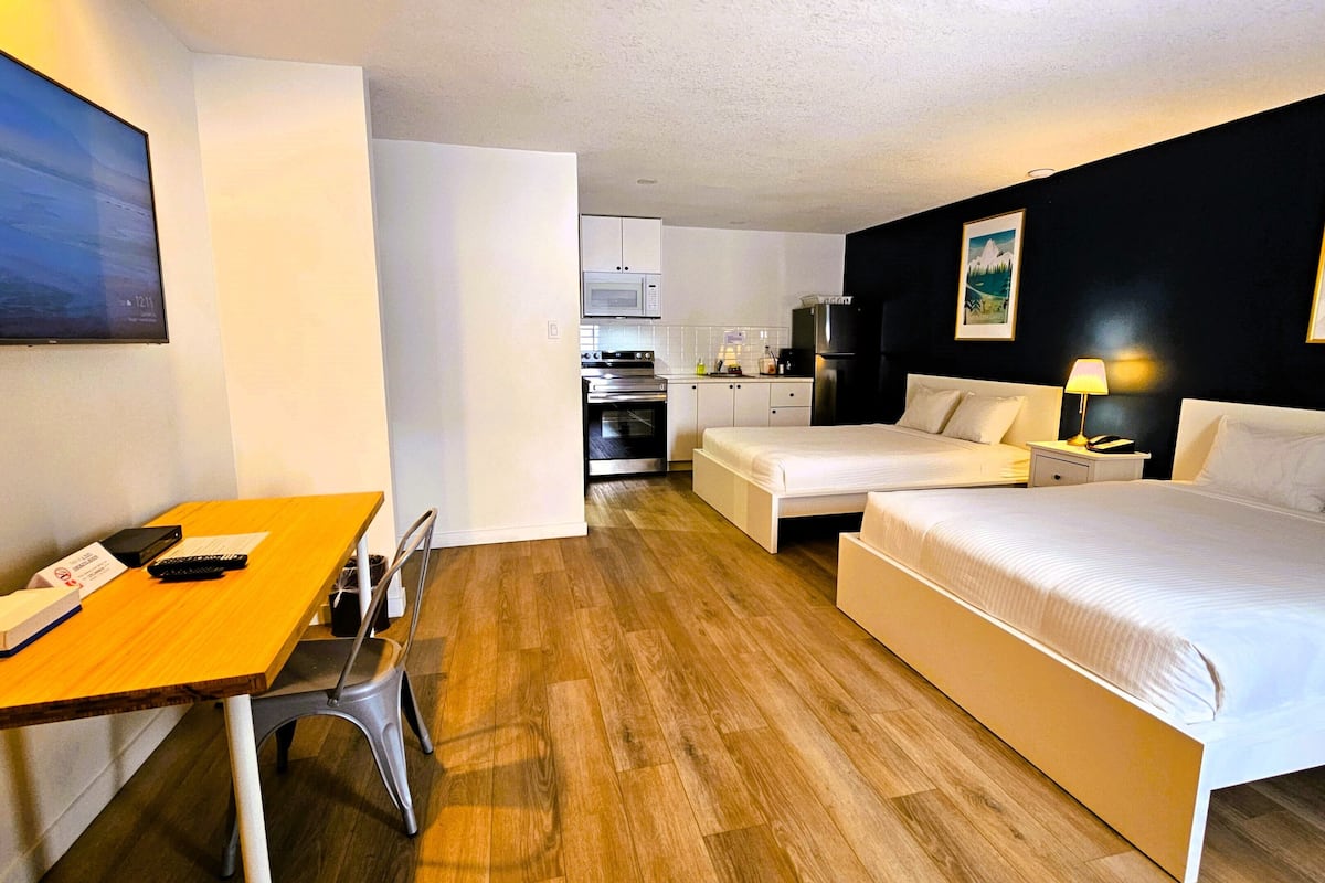 A hotel room with two beds, a dining table, a kitchen area, and a TV.