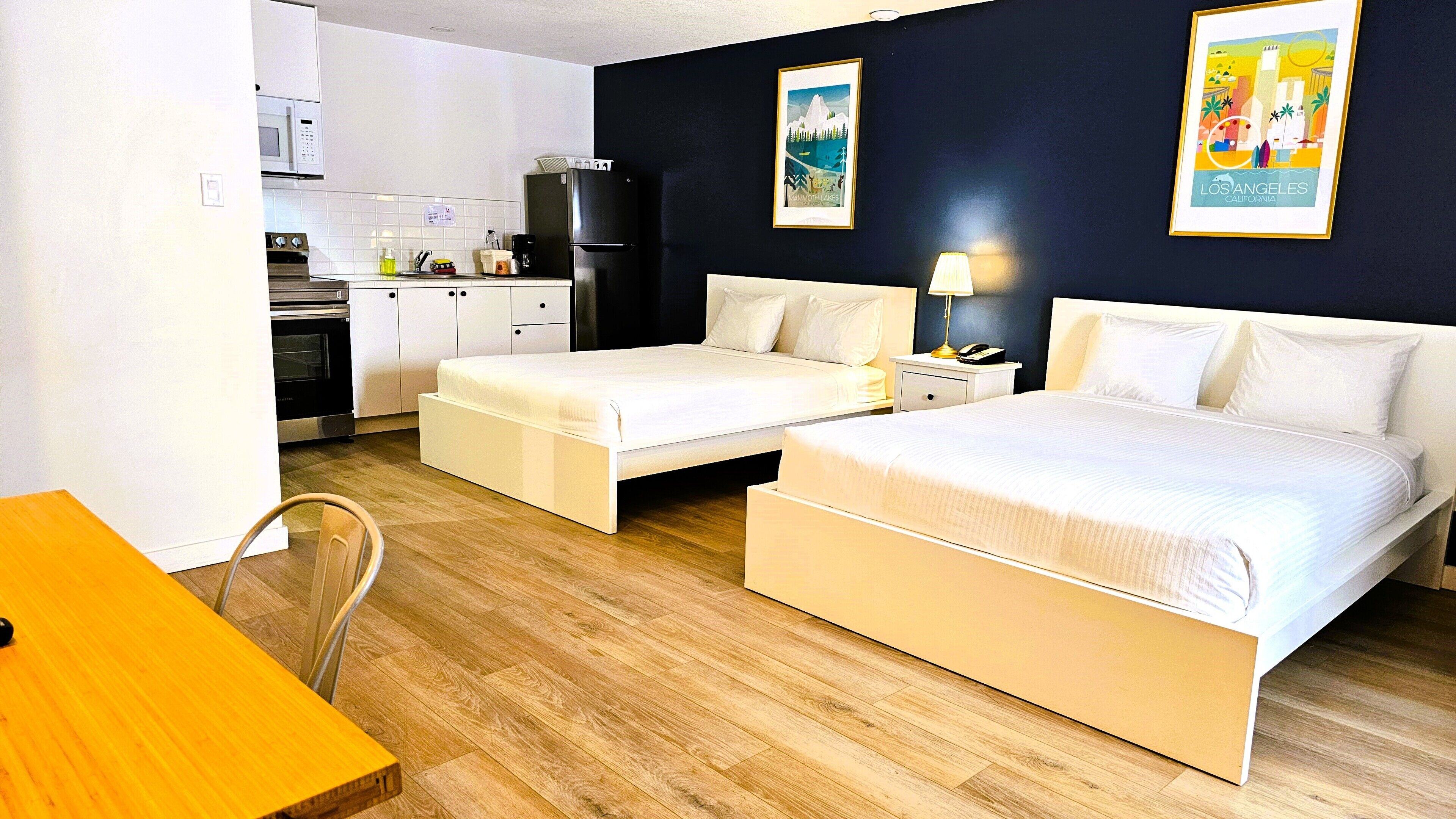 A hotel room with two beds, a small kitchenette, and a dining area.