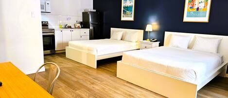 A hotel room with two beds, a small kitchenette, and a dining area.
