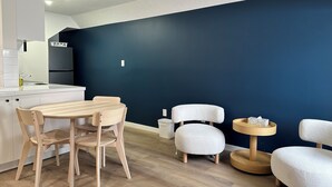 A modern kitchen with white cabinets and a dark blue accent wall. There is a wooden dining table with four chairs and a small round table with a bowl. - Cloud 9 Inn (Whitecourt)