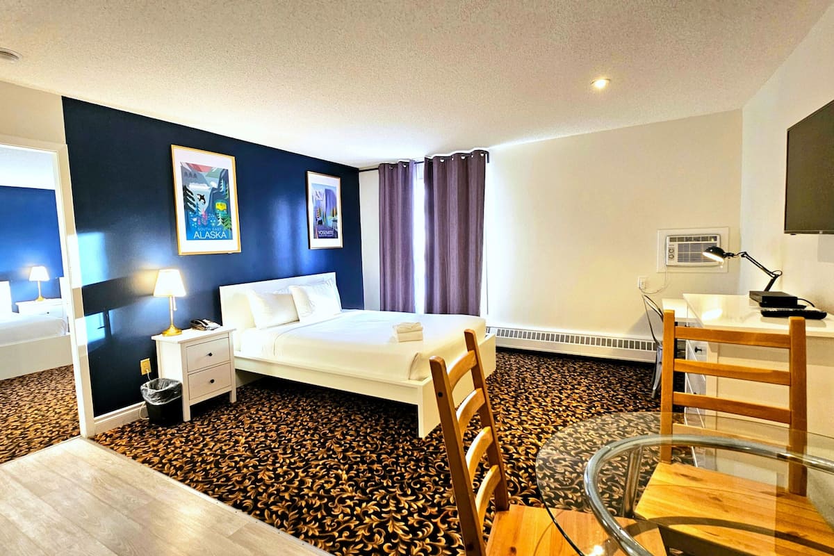 A hotel room with a bed, bedside tables, a desk, a chair, and a TV.